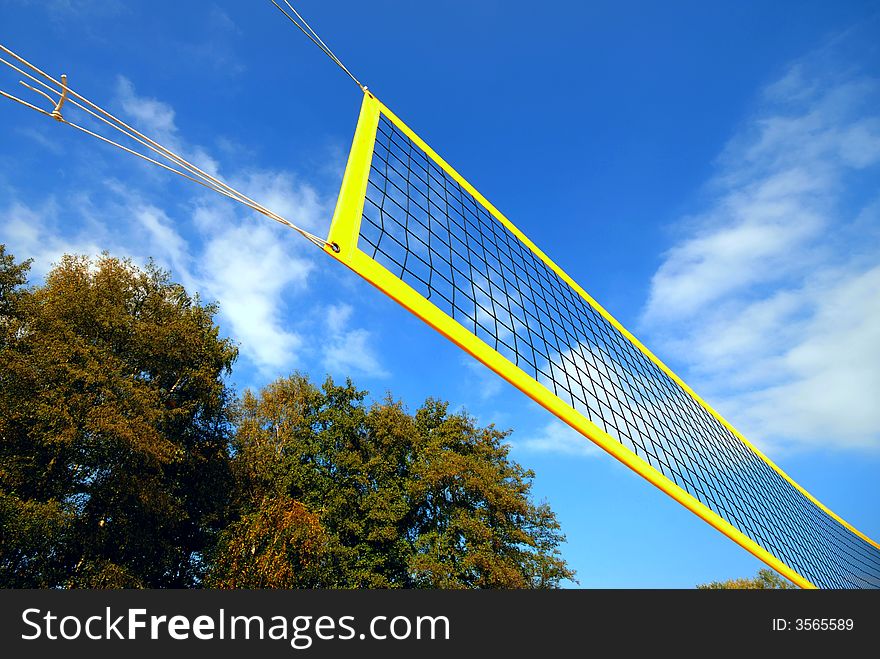 Yellow volleyball net under blue clouded sky, in the background autumn trees