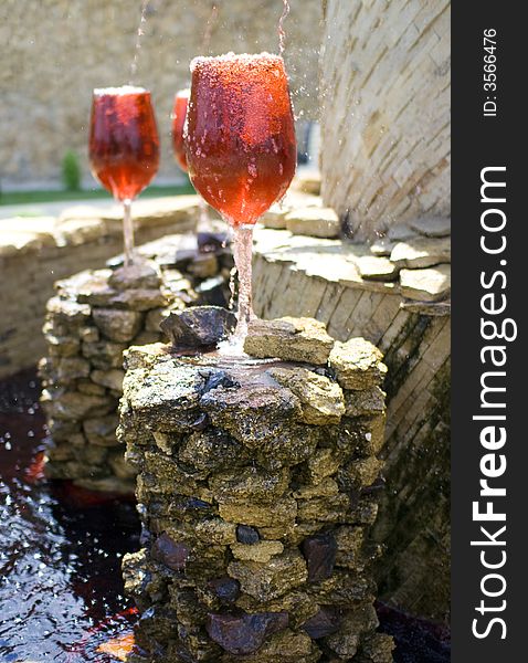 Fountain with red wine pouring into huge glasses on stones. Fountain with red wine pouring into huge glasses on stones.