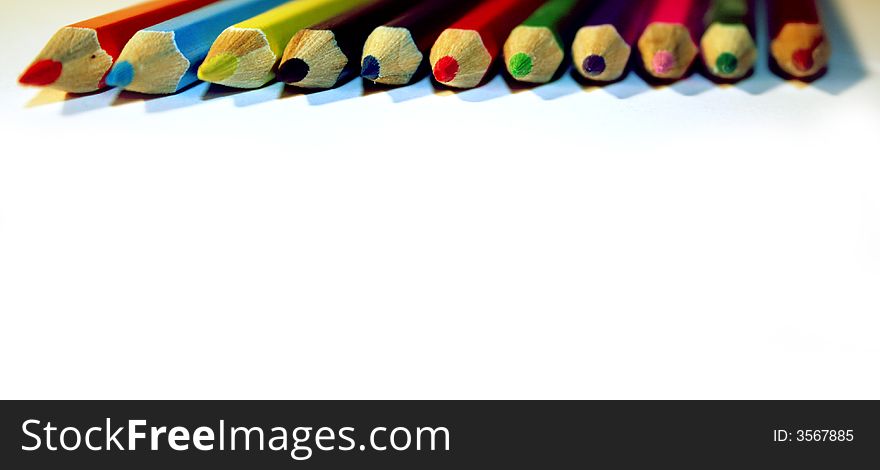 A line of wooden colored wooden pencils on a white ground. A line of wooden colored wooden pencils on a white ground.