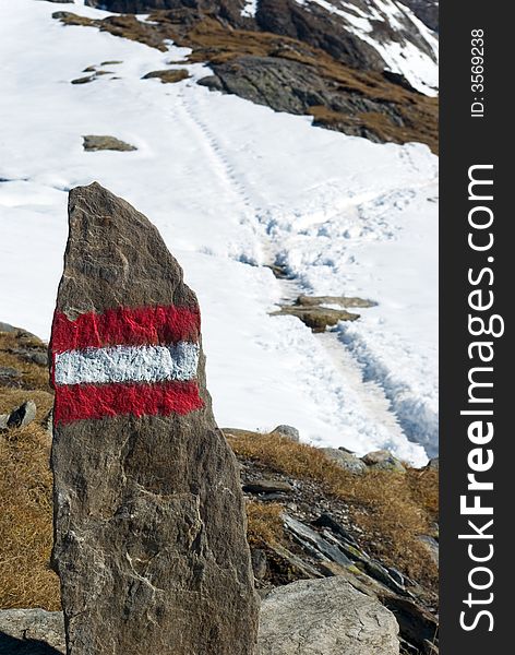 Red marking on stone, in background footpath in snow, Alps