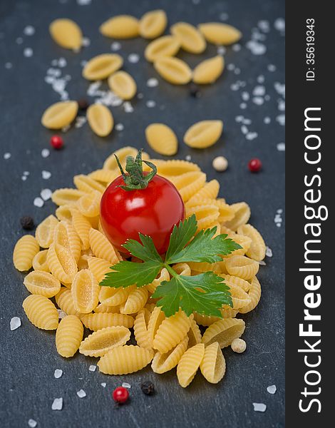 Italian pasta shells, cherry tomatoes, salt and pepper on a dark background, vertical