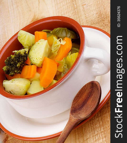 Rustic Vegetable Stew with Broccoli, Carrot, Leek and Potato in Beige Bowl with Wooden Spoon closeup on Wooden background. Rustic Vegetable Stew with Broccoli, Carrot, Leek and Potato in Beige Bowl with Wooden Spoon closeup on Wooden background