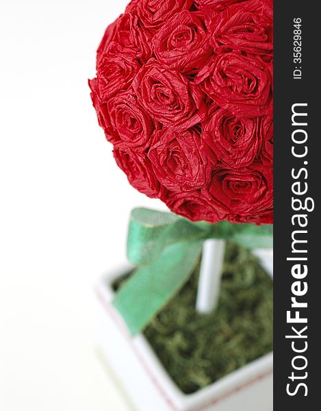 Close-up of red crepe paper rose topiary with green ribbon and moss.