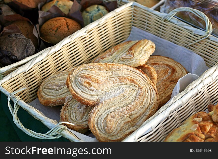 A wicker basket with fresh-baked pastries at a local farmer's market. A wicker basket with fresh-baked pastries at a local farmer's market