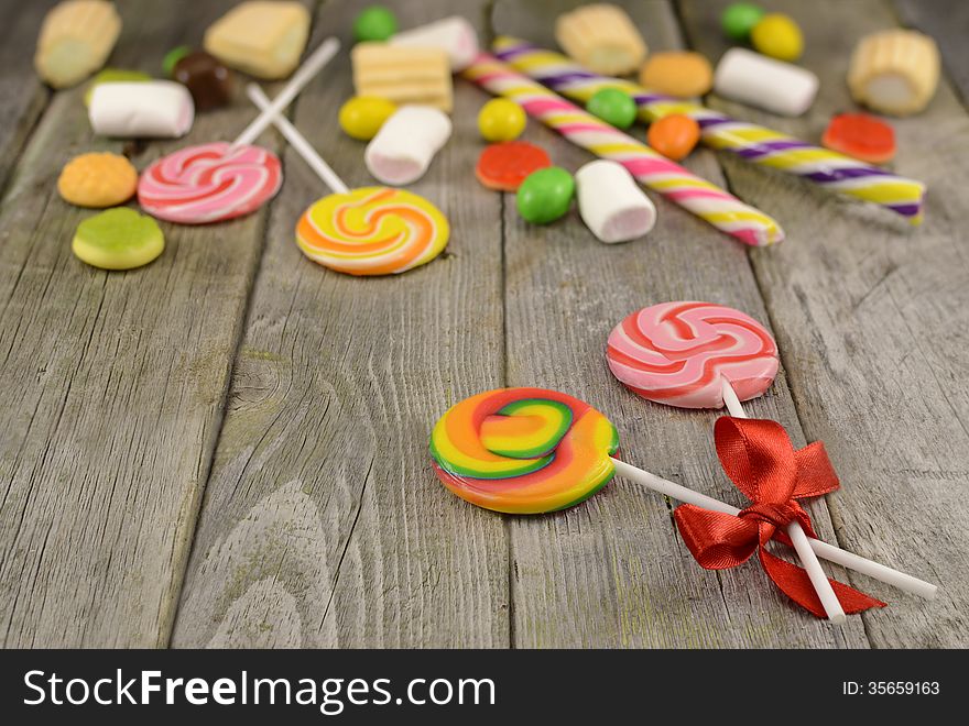 Pair of colorful lollipops and pile of sweet goods on wood. Pair of colorful lollipops and pile of sweet goods on wood