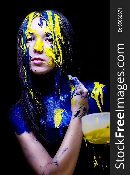 Beauty/fashion close up portrait of woman painted blue and yellow with brushes and paint  on black background