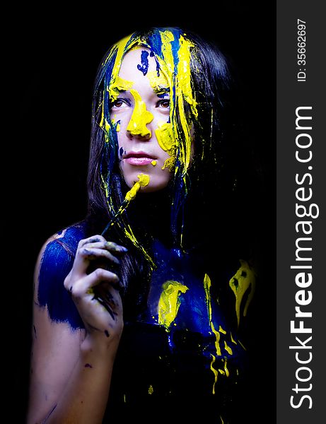 Beauty/fashion close up portrait of woman painted blue and yellow with brushes and paint  on black background