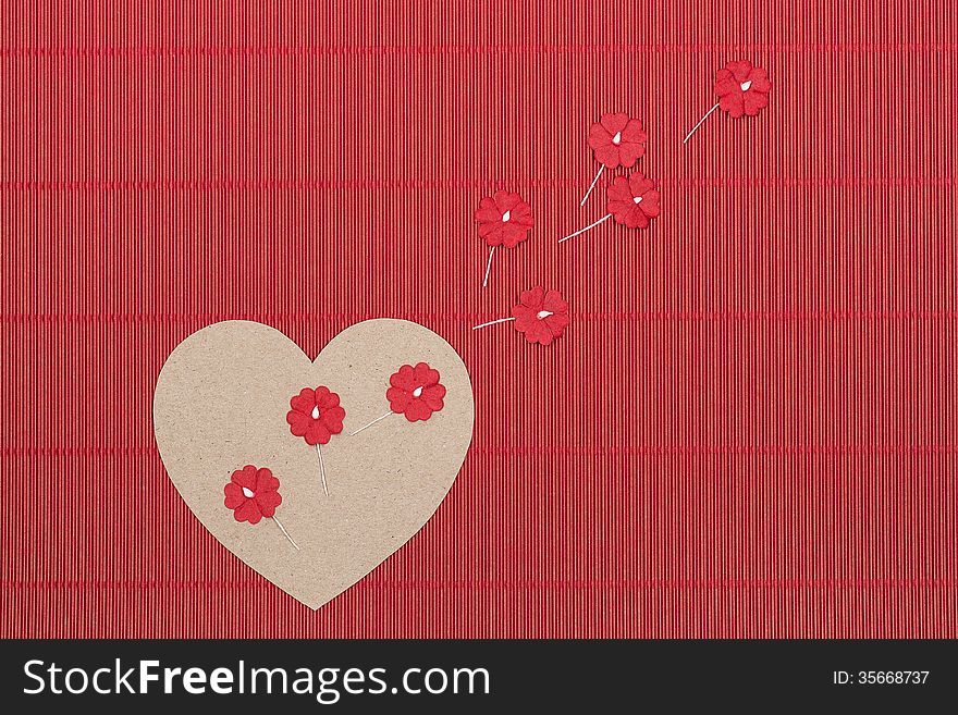 Cardboard heart with paper flowers on red corrugated background.