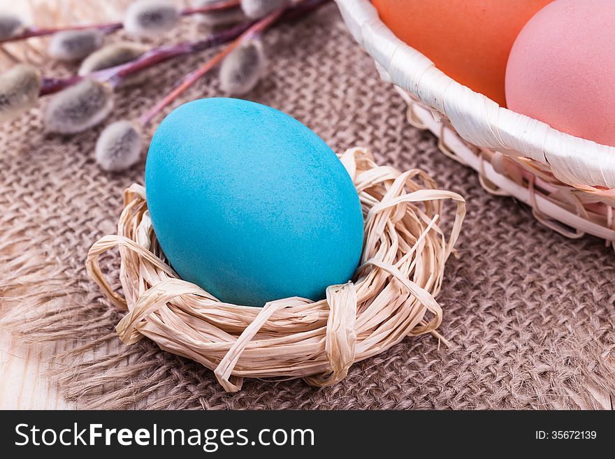 Easter egg in small nest with Easter basket and willow on wooden table