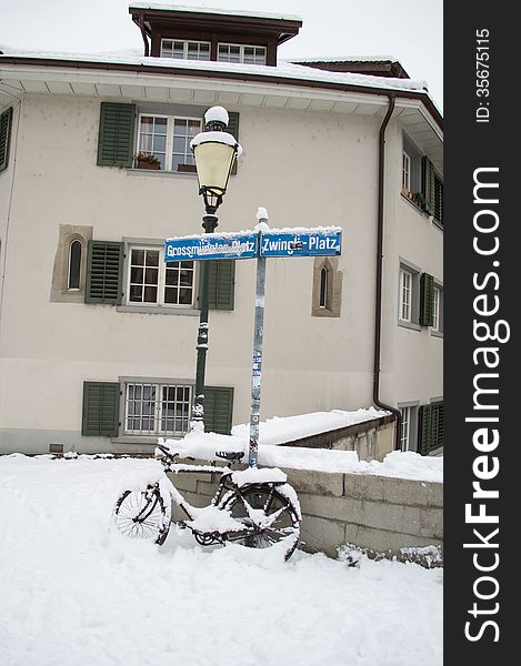 Light Street lamp with a bicycle covered by snow in a street under a signpost in Zurich, Switzerland. Light Street lamp with a bicycle covered by snow in a street under a signpost in Zurich, Switzerland