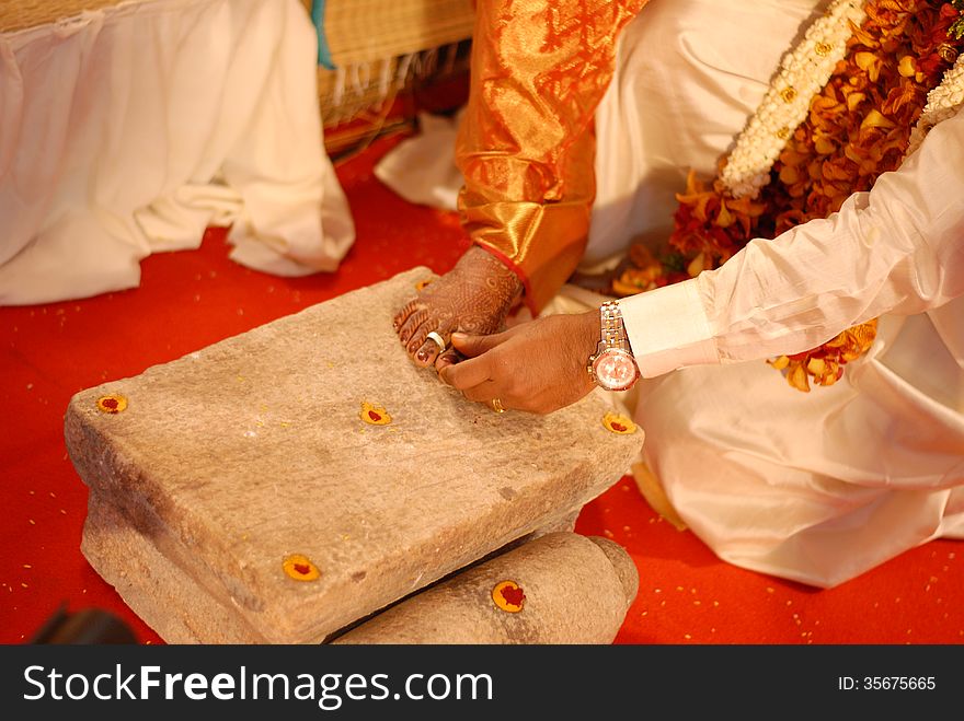 Bride groom is wearing a silver metti ring to the foot finger of bride placed on a grinding stone in a wedding function. Bride groom is wearing a silver metti ring to the foot finger of bride placed on a grinding stone in a wedding function