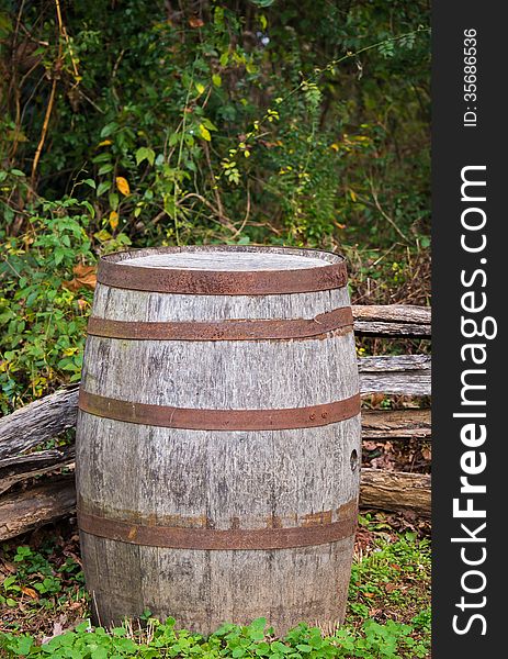 A vertical shot of an old and rustic barrel sitting in the corner of an old wooden fence. A vertical shot of an old and rustic barrel sitting in the corner of an old wooden fence.