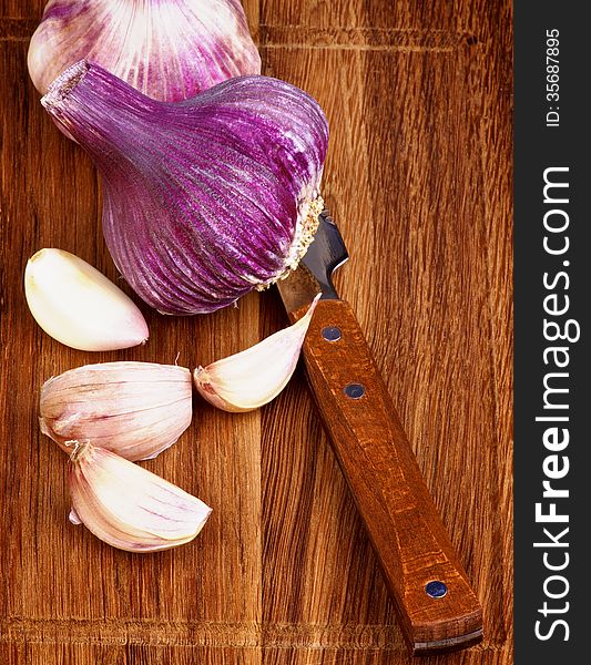 Arrangement of Fresh Pink Garlic Full Body and Slices with Kitchen Knife on Wooden Cutting Board closeup