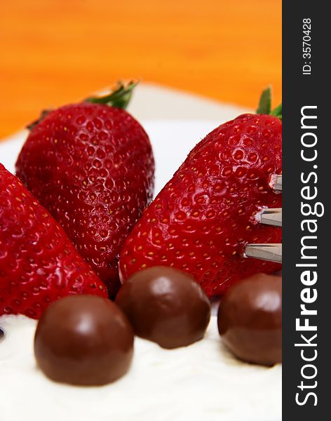 Three strawberries with chocolate balls lying in cream on white saucer. Three strawberries with chocolate balls lying in cream on white saucer