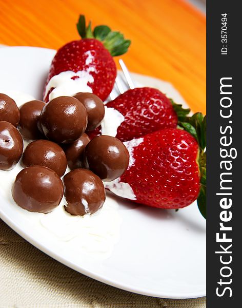 Three strawberries with chocolate balls lying in cream on white saucer. Three strawberries with chocolate balls lying in cream on white saucer