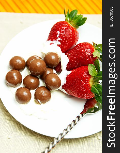 Three strawberries with chocolate balls lying in cream on white saucer. Three strawberries with chocolate balls lying in cream on white saucer