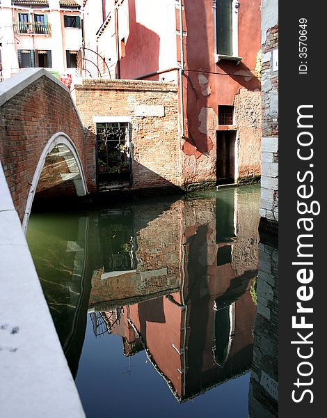 Pink Stucco wall and bridge reflection over small canal in Venice, Italy
