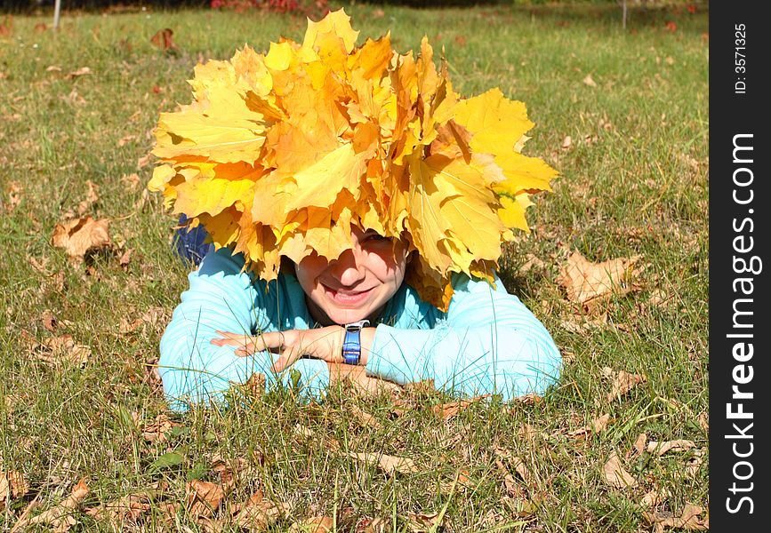 Portrait of the girl in a chaplet from yellow maple leaves lies in a grass