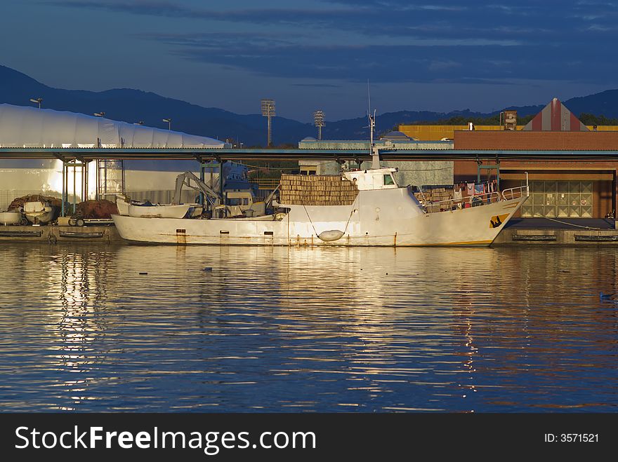 Fishing boat are at rest in an italian port at golden hour. Beautiful gold sunny reflection