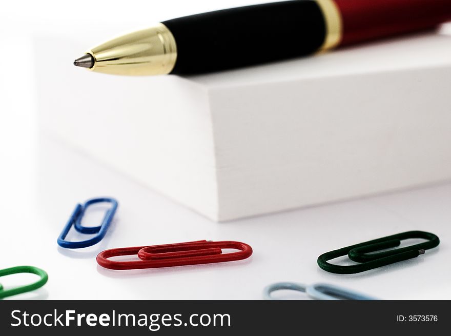 Pen on top of post-it cube with colored paper clips isolated on white. Pen on top of post-it cube with colored paper clips isolated on white