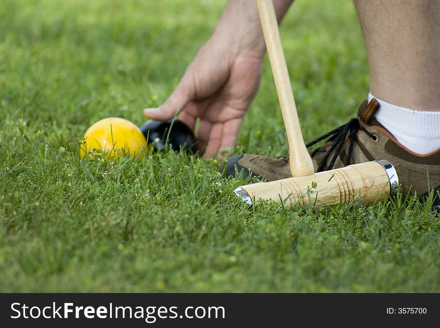 Man placing a black croquet ball behind a yellow ball to hit it out of the playing field. Man placing a black croquet ball behind a yellow ball to hit it out of the playing field.