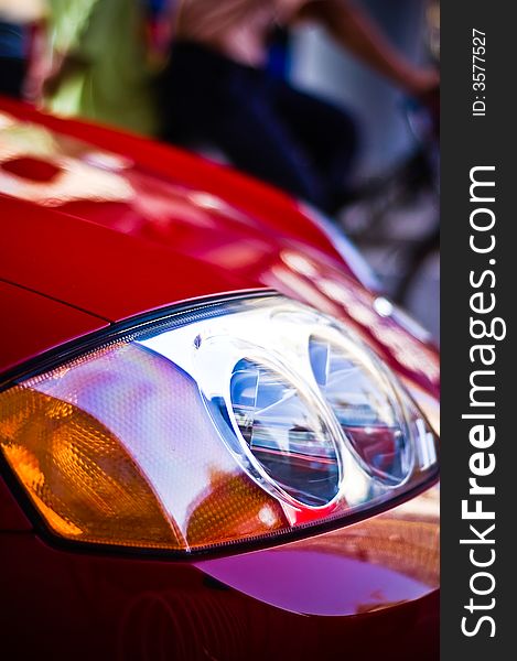 Vibrant crop of the front headlight of a red sports car. Features narrow depth-of-field and an interesting bokeh in the background. Vibrant crop of the front headlight of a red sports car. Features narrow depth-of-field and an interesting bokeh in the background.