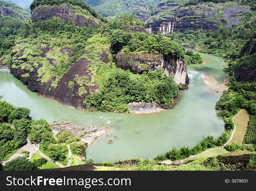 River around a huge rocky hill covered by green bushes. River around a huge rocky hill covered by green bushes.