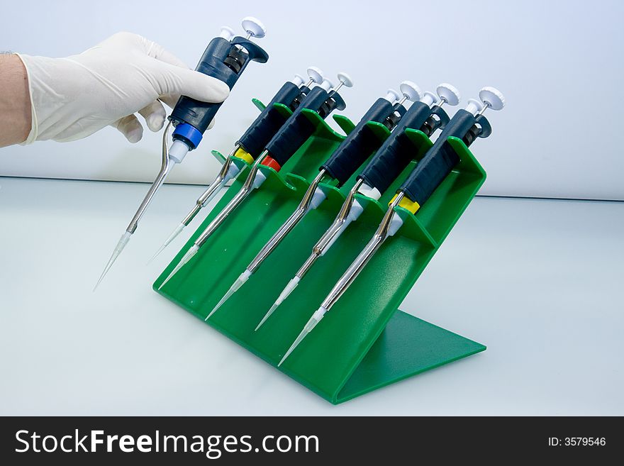 Set of mechanical pipettes in a green plastic holder, one pipette is taken by the research assistant. Set of mechanical pipettes in a green plastic holder, one pipette is taken by the research assistant