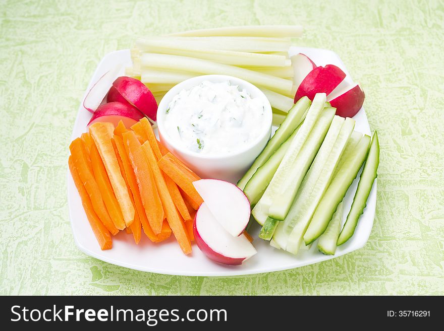 Sauce with feta cheese and assorted vegetables on a plate on green background, close-up