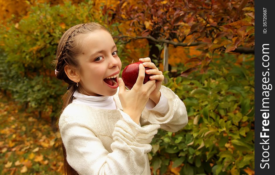 Beautiful girl biting a red apple on the background of the autumn landscape. Beautiful girl biting a red apple on the background of the autumn landscape