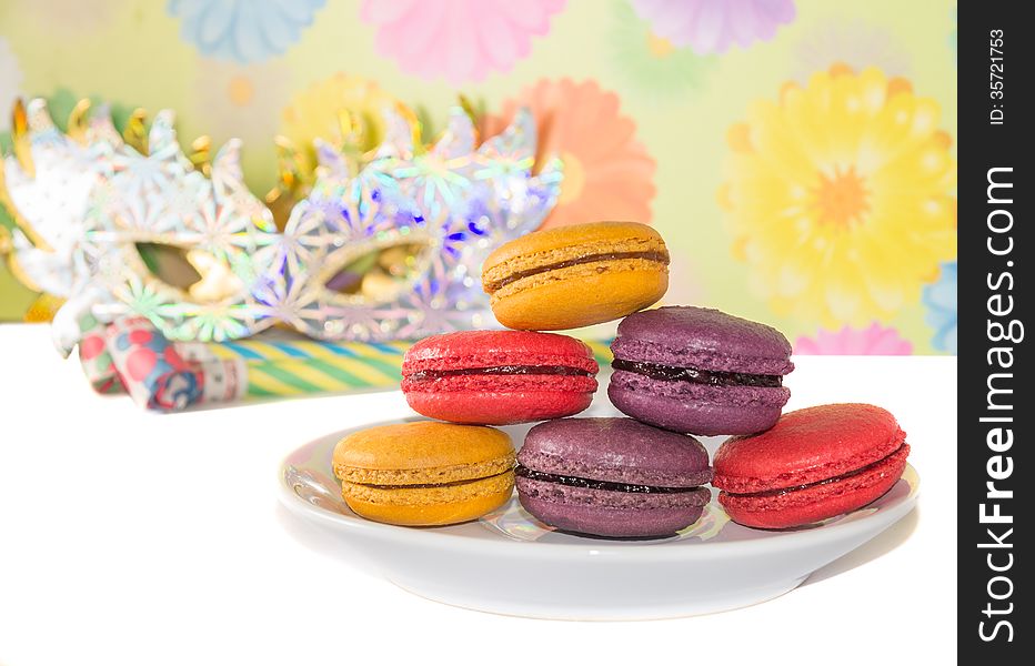 Sweet colorful macaron against festive masks and pipes