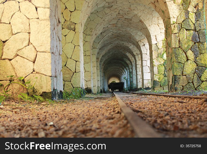 Old mining railway going through a stone tunnel with vegetation growing on the stone pylons and gravel under train tracks