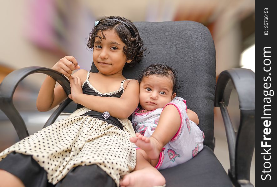 Two siblings brother & sister playing together while sitting on chair inside home. Two siblings brother & sister playing together while sitting on chair inside home