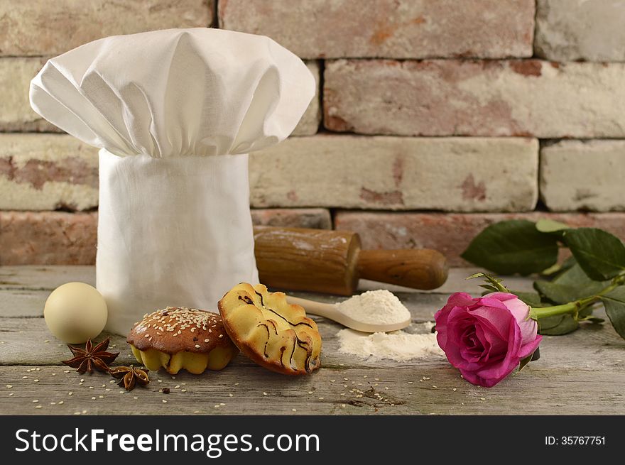 White toque with bakery, rolling pin and pink rose on brick wall. White toque with bakery, rolling pin and pink rose on brick wall