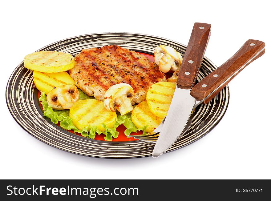 Roasted Turkey Steak Garnished with Grilled Sliced Potato, Portabello Mushrooms, Lettuce on Striped Plate with Fork and Knife isolated on white background