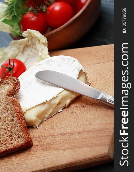 Camembert and knife on cutting board near vegetables. Camembert and knife on cutting board near vegetables
