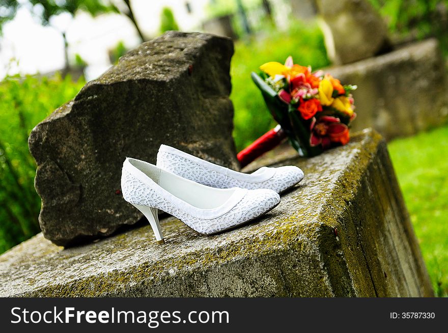 Wedding shoes with bride bouquet on a stone background