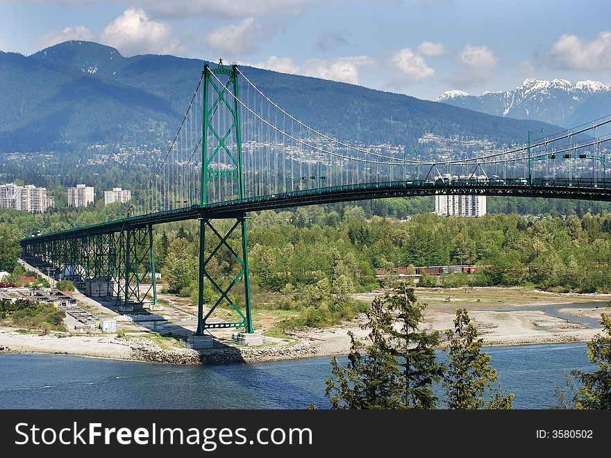 The view from Stanley's park of Lion Gates bridge with East Vancouver and mountains in a background (British Columbia, Canada). The view from Stanley's park of Lion Gates bridge with East Vancouver and mountains in a background (British Columbia, Canada).