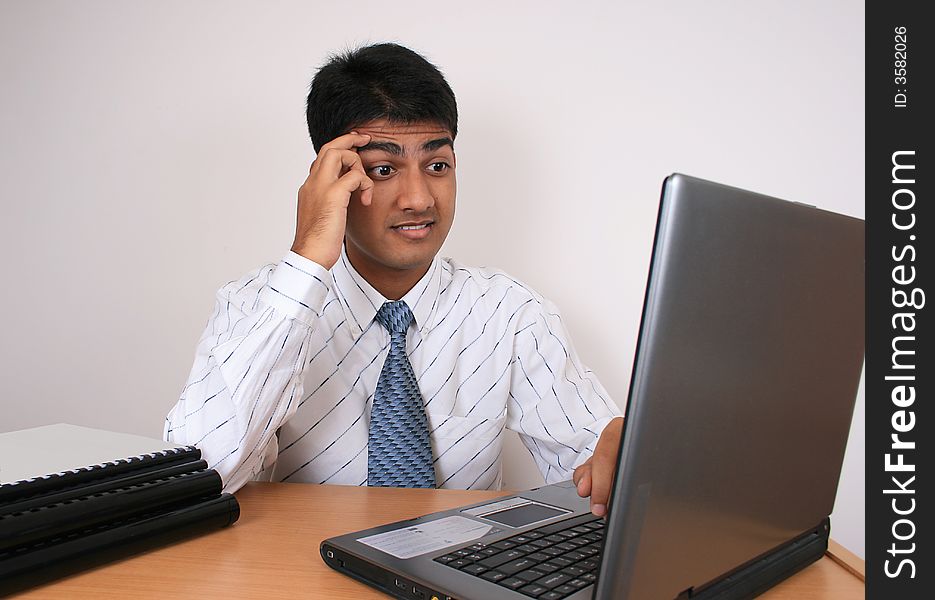 Young Indian business man working at his desk. Has a puzzled look.(Series). Young Indian business man working at his desk. Has a puzzled look.(Series)