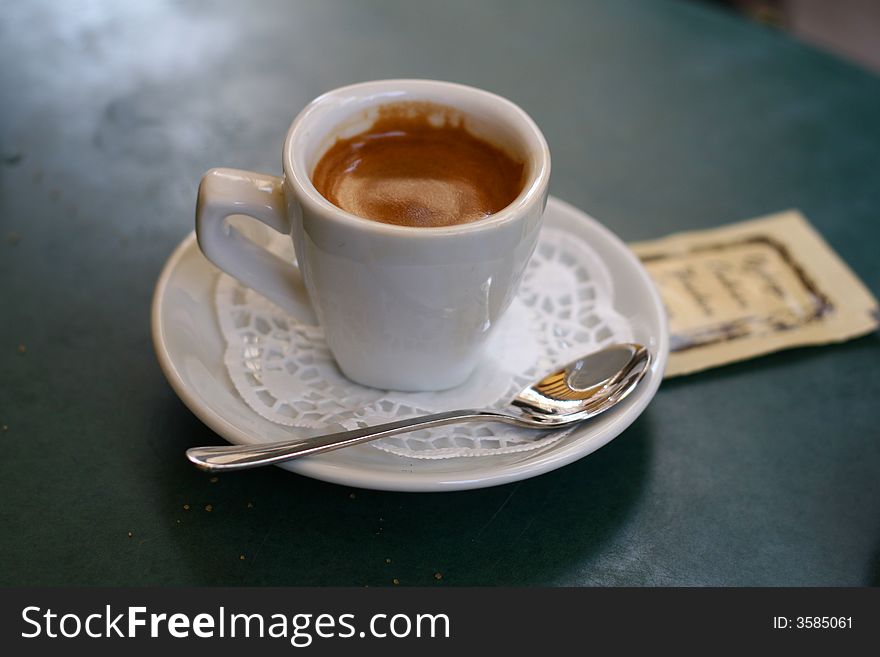 White cup of coffee with a ferrous spoon on a green table