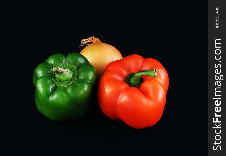 A yellow onion and Red and green bell peppers against a black background. A yellow onion and Red and green bell peppers against a black background.