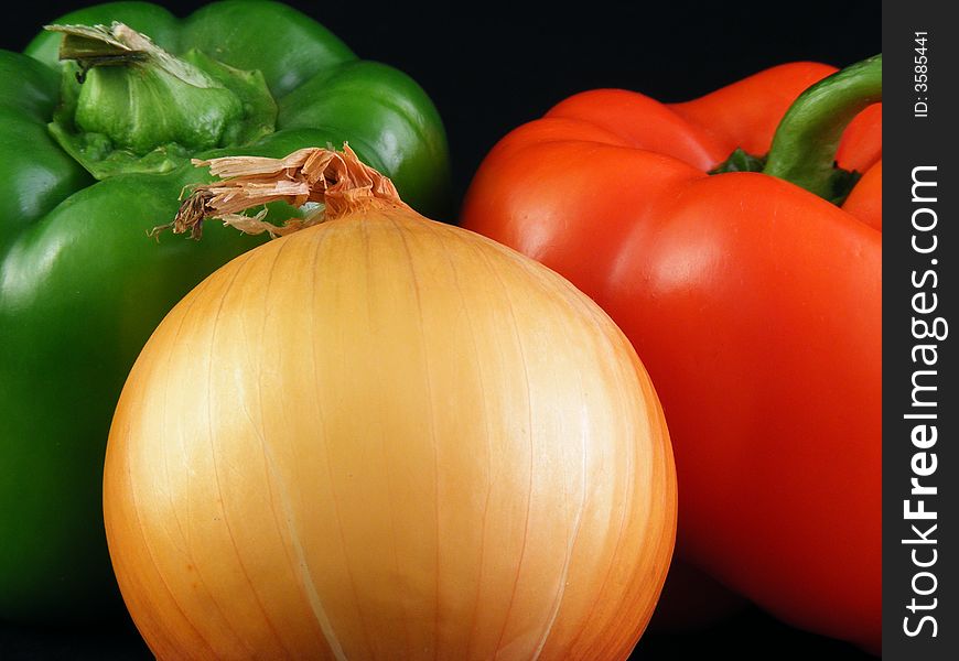 A yellow onion and Red and green bell peppers against a black background. A yellow onion and Red and green bell peppers against a black background.