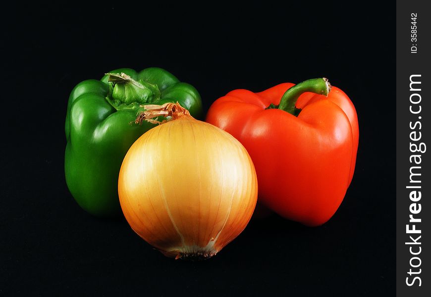 A yellow onion and Red and green bell peppers against a black background. A yellow onion and Red and green bell peppers against a black background.