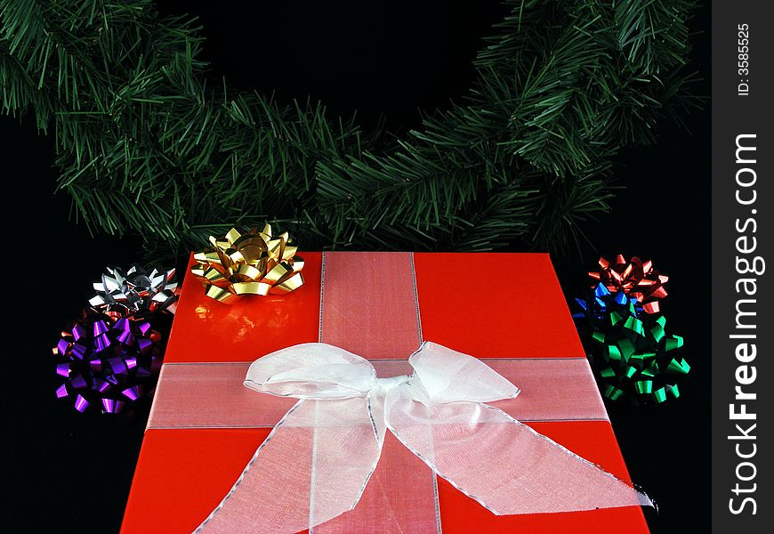 A christmas gift with a ribbon and a bow with a wreath in the background.