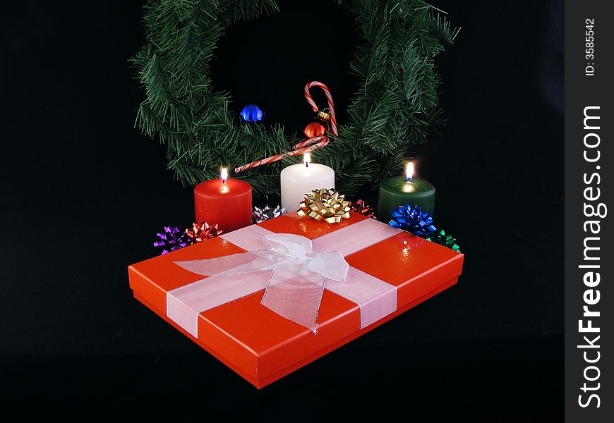 A christmas gift with a ribbon and a bow with a wreath in the background.