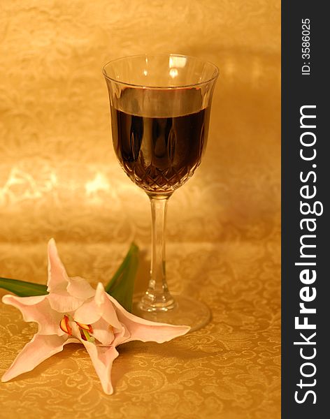 Glass of red wine on golden background and a white lilly next to it. Glass of red wine on golden background and a white lilly next to it