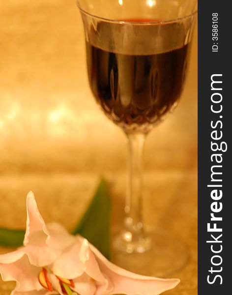 Glass of red wine on golden background and a white lilly next to it. Glass of red wine on golden background and a white lilly next to it