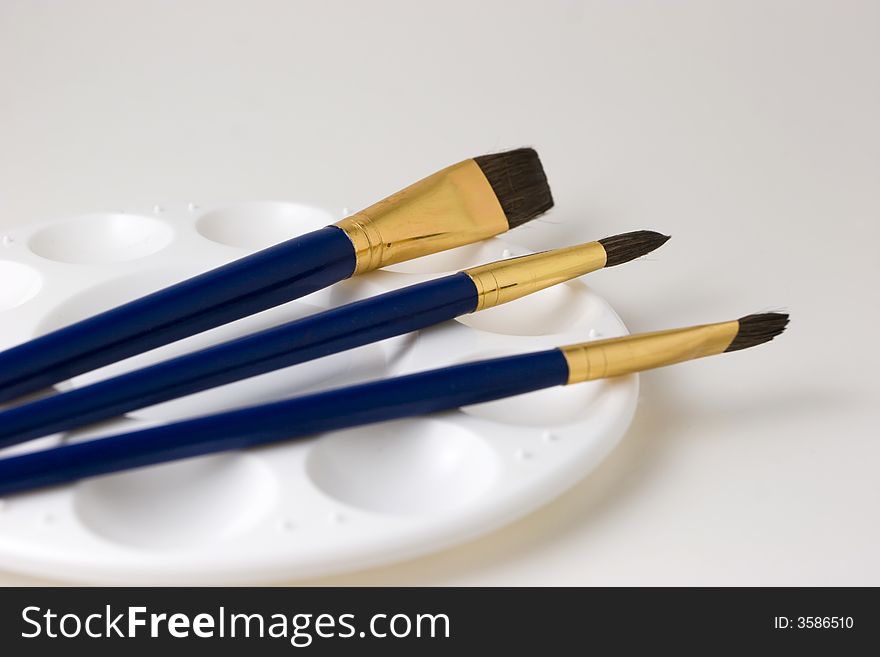 Three blue artist brushes on top of an empty paint palette with a white background. Three blue artist brushes on top of an empty paint palette with a white background.