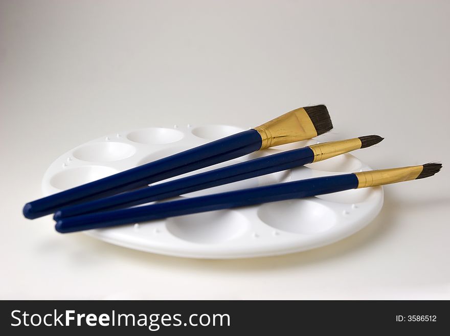 Three blue artist brushes on top of an empty paint palette with a white background. Three blue artist brushes on top of an empty paint palette with a white background.