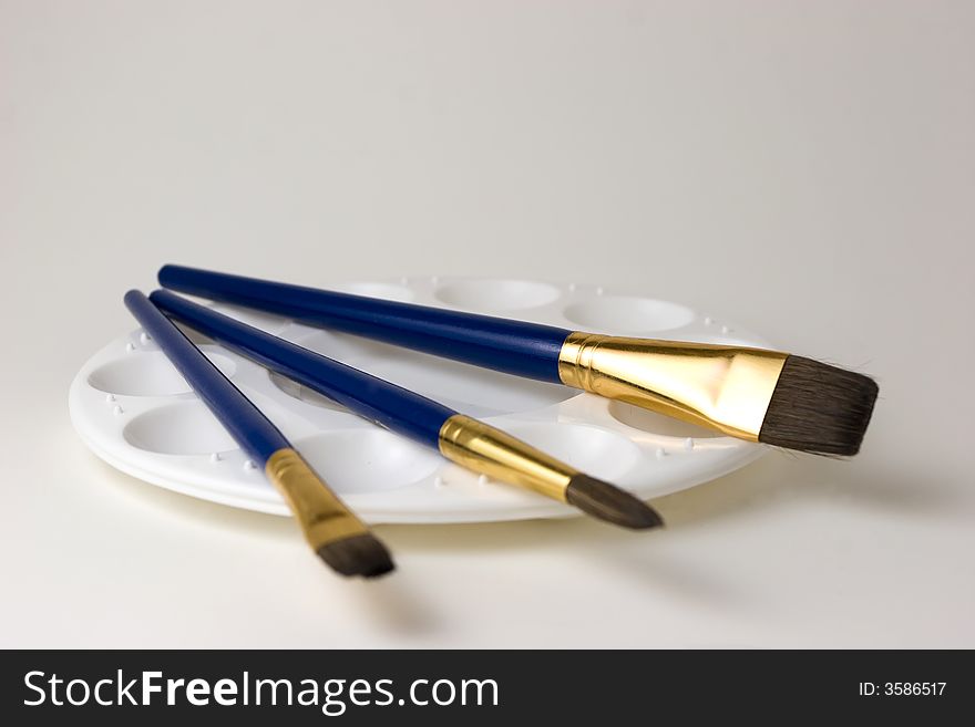 Three blue artist brushes on top of an empty paint palette with a white background. Three blue artist brushes on top of an empty paint palette with a white background.